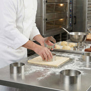 Person in a kitchen using a metal ring to cut dough on a floured surface.