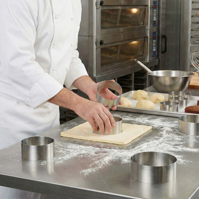 Person in a kitchen using a metal ring to cut dough on a floured surface.