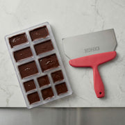 Chocolate mold with filled molds and a spatula on a marble surface