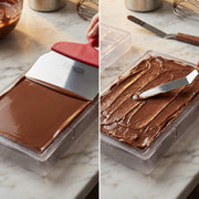 Chocolate being spread into a mold with a spatula on a marble surface.