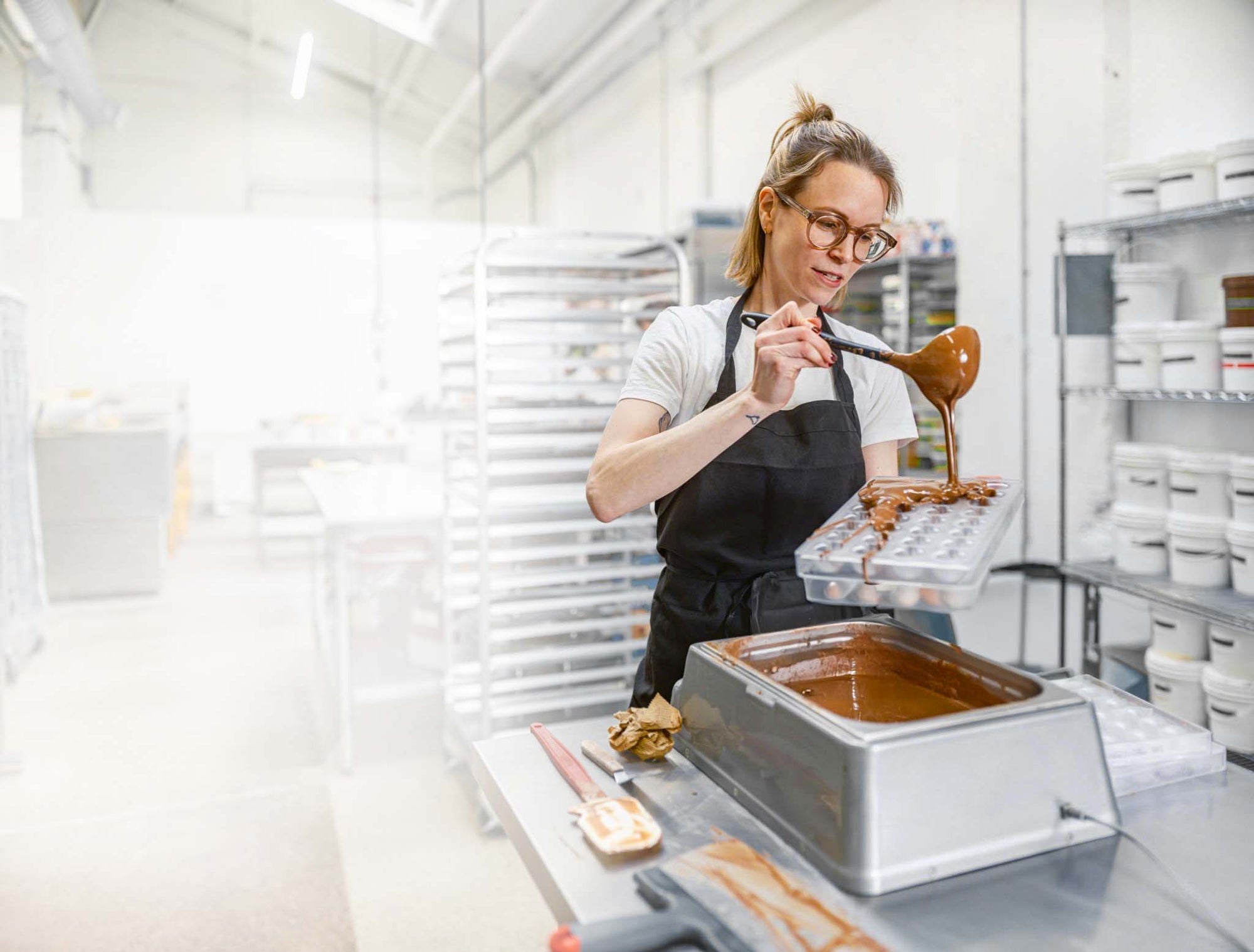 Professional Women Chocolatier using melted chocolate with chocolate mold and melting chocolate machine.