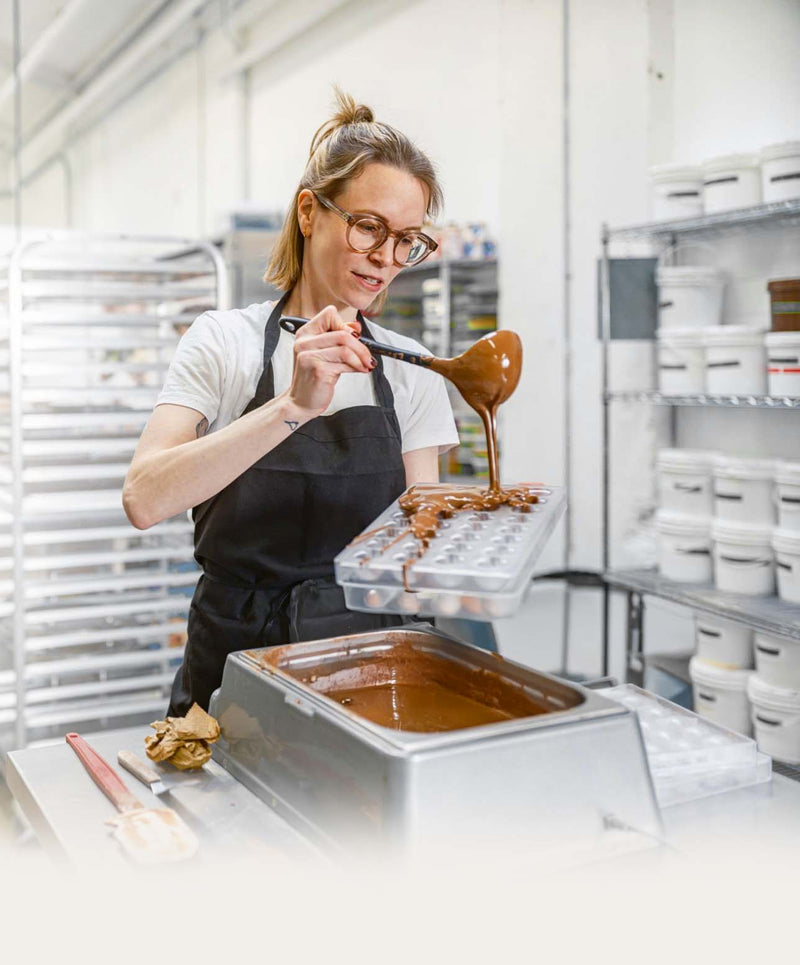 Professional Women Chocolatier using melted chocolate with chocolate mold and melting chocolate machine.